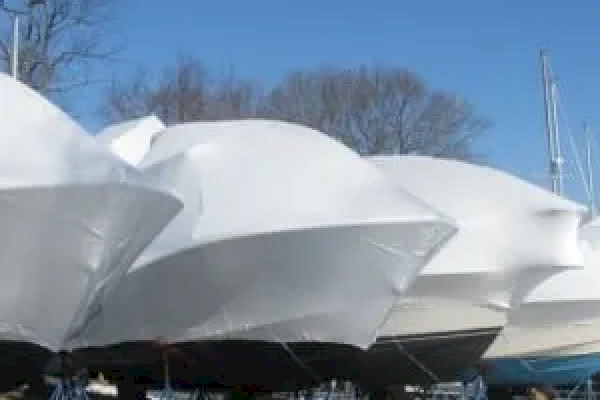 This image shows several boats covered in white shrink wrap, likely in dry storage for the winter, with a clear blue sky in the background.